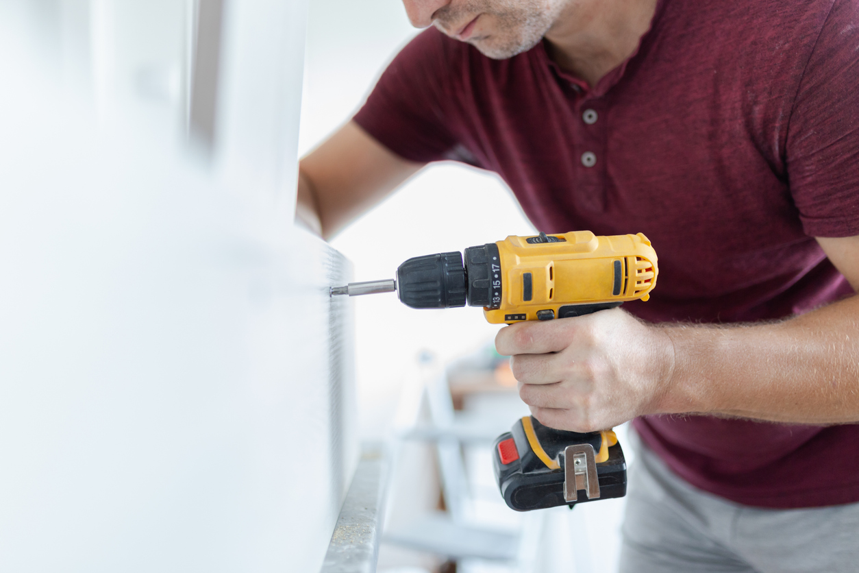 Carpenter installing kitchen chest of drawers by using electrical screwdriver. Home renovation concept.