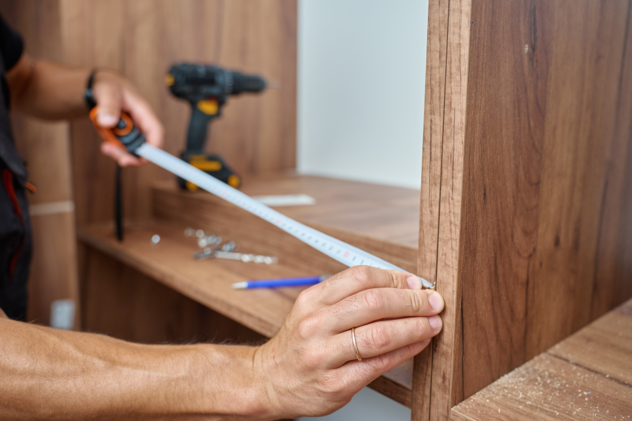 Man measuring wooden wardrobe with tape measure, Furniture assembling process